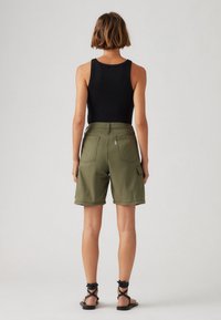 Pantalones cortos de carga caquí con dos bolsillos traseros y un bolsillo lateral, combinados con una camiseta sin mangas negra y sandalias negras con tiras.