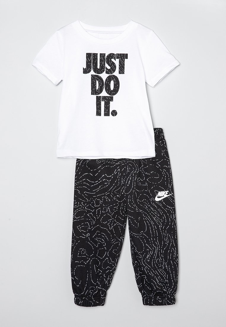 Biała koszulka bawełniana z czarnym napisem "JUST DO IT." w połączeniu z czarnymi spodniami dresowymi z białymi abstrakcyjnymi wzorami oraz logo Nike.