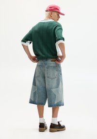 Grøn stribet kortærmet sweater, lys blå denimshorts med stjernemønster, mørke sko og lyserød kasket. Model positioneret fra bagfra.
