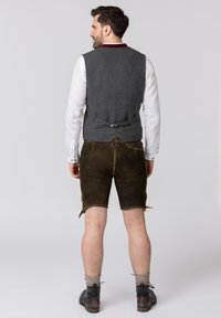 Grau gestrickte Weste mit einem kastanienbraunen Kragen, kombiniert mit braunen Leder-Shorts mit seitlichen Verschlüssen, getragen mit schwarzen Stiefeletten und grauen Socken.