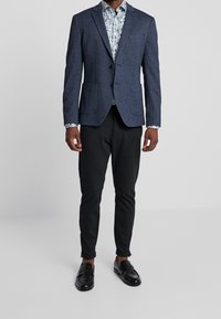 Námořnický blazer s dvěma knoflíky, dvěma předními kapsami, zkombinovaný s vzorovanou košilí a černými zúženými kalhotami. Čern�é mokasíny dokončují outfit.