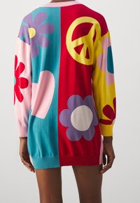 Maglione oversize multicolore, con motivi floreali, simbolo della pace e design a forma di cuore su sezioni vivaci di rosso, rosa, giallo e blu.