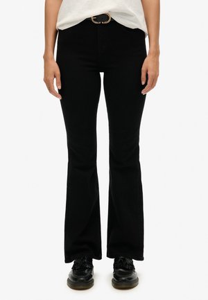 Jean negros de campana con una textura suave, ajuste de cintura alta y cinturón con hebilla dorada. Combinados con zapatos negros. Sin patrones o acentos visibles.