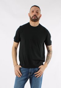 Maglione nero a maniche corte in maglia con scollatura rotonda, dalla texture liscia e design aderente, abbinato a jeans in denim blu.