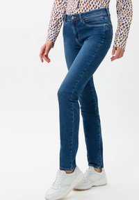 Modré džíny z denimu ve slim fit, s středně vysokým pasem, designem pěti kapes a jemným vyblednutím; v kombinaci s bílými teniskami.