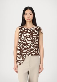 Top senza maniche beige e marrone a fantasia con scollo arrotolato e fiocco laterale, abbinato a pantaloni beige con vestibilità rilassata.
