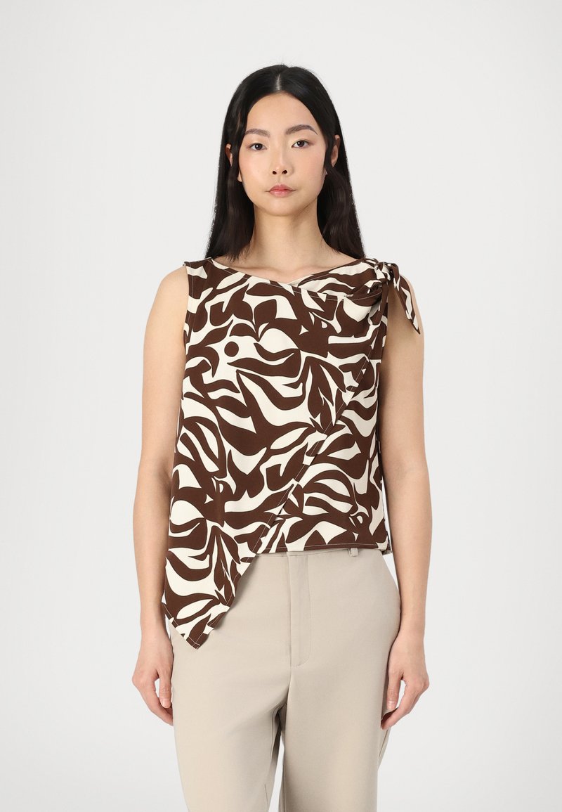 Top senza maniche beige e marrone a fantasia con scollo arrotolato e fiocco laterale, abbinato a pantaloni beige con vestibilità rilassata.