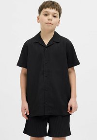 Camisa negra de botones de manga corta con cuello, con rayas verticales. Combinada con pantalones cortos negros a juego, ambos en una tela texturizada.
