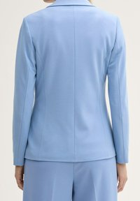 Lichtblauwe op maat gemaakte blazer met een soepele textuur, gestructureerde pasvorm en notch revers. De achterkant heeft een centrale naad en een getailleerd silhouet.