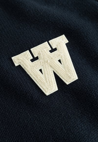 Tissu en maille bleu marine avec un grand logo "W" blanc texturé et bien en évidence. Détails fins des coutures et du motif tissé visibles.