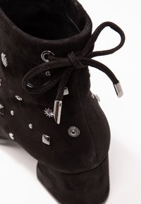 Stivaletto alla caviglia in suede nero con borchie in metallo e decorazioni a forma di stella, dotato di un fiocco legato con estremità metalliche su un lato.