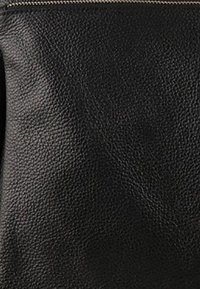 Sac en cuir noir avec une finition texturée et une fermeture éclair sur le dessus. Le matériau semble durable et légèrement granuleux, adapté à un usage quotidien.