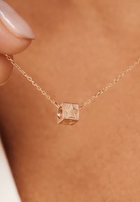 Collier en or rose avec un pendentif cubique au design étoilé, accompagné d'une chaîne délicate et d'une texture lisse.