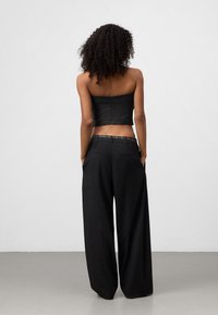 Zwarte cropped top met een textuur en een rits aan de achterkant, gecombineerd met brede zwarte broek met zakken en een geruite tailleband.