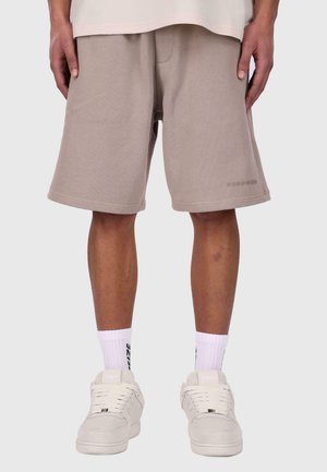 Beige cotton shorts with side pockets and a relaxed fit, paired with white sneakers and crew socks featuring black text.