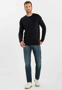 Camiseta negra de manga larga con cuello redondo, combinada con vaqueros azules y zapatillas blancas con suelas marrones; textura lisa, diseño ajustado.