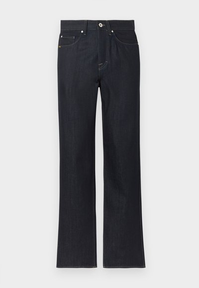 Tumesinised sirgebäärilised teksapüksid ees taskute, nööpide kinnituse ja nähtavate õmblustega lihtsal heledal taustal.