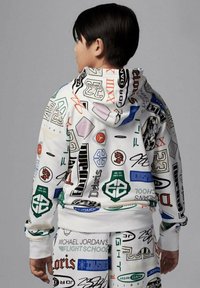 Felpa con cappuccio e pantaloni in tessuto bianco coperti da logo e testi colorati. Presenta un cappuccio con cordino e polsini a coste.