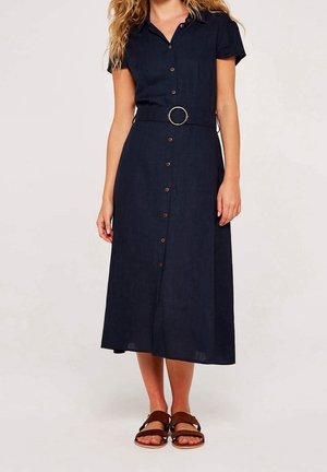 Femme portant une robe midi bleu marine à manches courtes avec des boutons sur le devant, une ceinture à boucle ronde et des sandales marron à double strap.