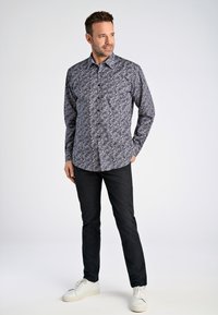 Skjorta med knappar i marinblått med små blommönster i lila och vitt. Matchad med svarta byxor och vita sneakers.