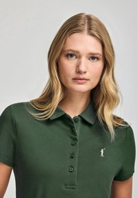 Zielona koszulka polo z kołnierzykiem i krótkimi rękawami. Posiada guzikowy zapięcie i małą emblemat na lewej piersi. Teksturowana tkanina.