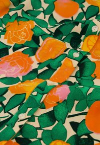 Stof met bloemmotief met oranje en roze rozen, groene bladeren op een crèmekleurige achtergrond. Bevat witte knopen en heeft een gladde textuur.