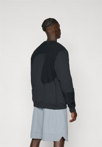 Black sweatshirt with textured back panel, ribbed cuffs, and hem. Worn with light gray shorts featuring a split hem design.