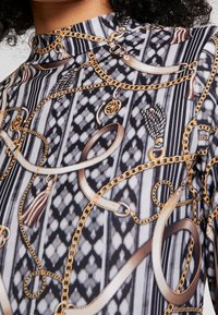 Svartvitt mönstrat tyg med guldkedjor, flätor och intrikata mönster. Hög hals med en slät, glänsande yta.