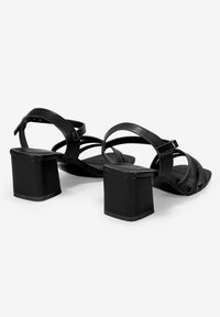 Sandalias de tacón negro con tacón cuadrado, que presentan múltiples tiras delgadas y una textura de cuero suave; hebilla ajustable para un ajuste seguro.