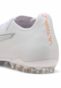 Weißer Fußballschuh mit strukturiertem Obermaterial, ausgestattet mit silbernen Akzenten und orangefarbenem "ULTRA"-Branding. Klare Gummistollen an der Sohle.