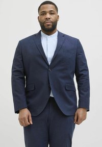 Dunkelblazer in Marineblau mit strukturierter Oberfläche, ausgestattet mit einer Brusttasche und zwei Fronttaschen, getragen über einem hellblauen Hemd mit Kragen.