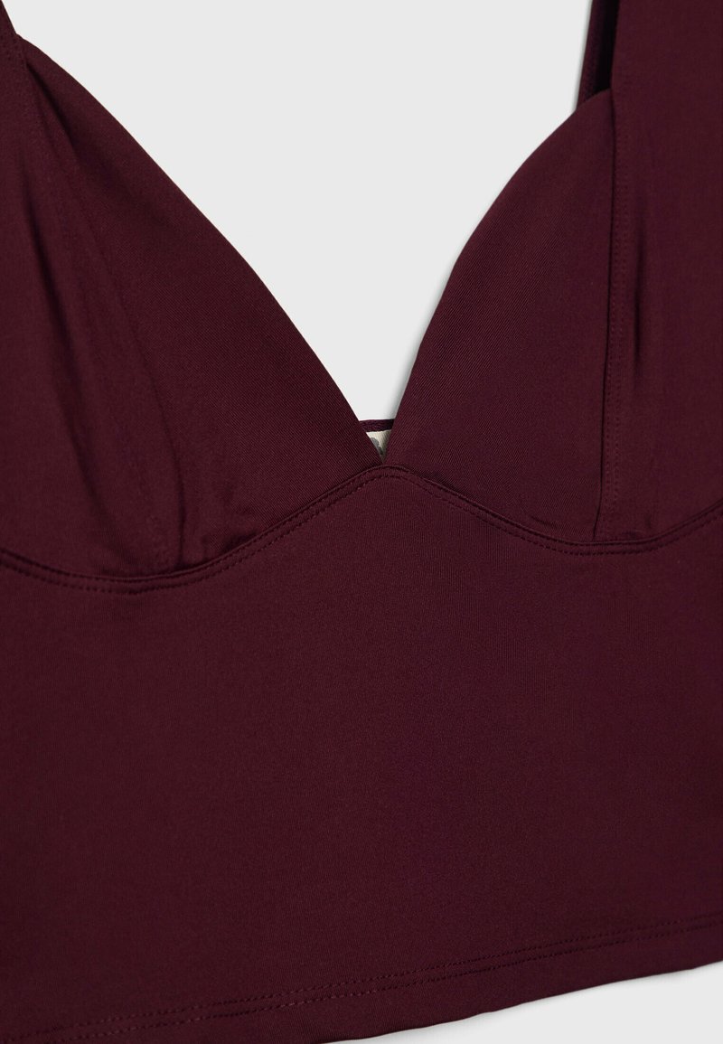 Top in pizzo bordeaux con design a V, in tessuto liscio e cuciture impunturate, che presenta un'estetica pulita e minimalista.