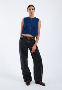 Top corto de mezclilla en azul oscuro con bordes sin rematar, combinado con unos pantalones negros de tiro alto y perneras anchas y zapatos de cuero marrón.