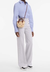 Chemise bleu clair à manches longues avec des boutons, pantalon large beige rayé, et un petit sac en osier beige avec des accents et détails marron. Baskets noires.