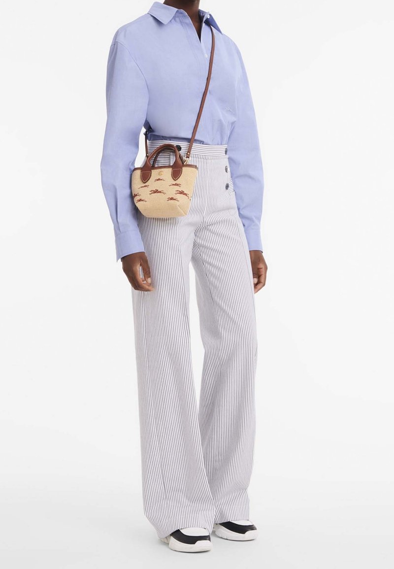 Chemise bleu clair à manches longues avec des boutons, pantalon large beige rayé, et un petit sac en osier beige avec des accents et détails marron. Baskets noires.