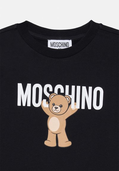 Svart bomull T-shirt med en central illustration av en björn med uppsträckta armar och varumärkesnamnet "MOSCHINO" i fetvita bokstäver ovanför.
