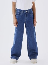 Blå denimbyxor med vida ben och hög midja, stora fickor och en urtvättad finish. Kombinationen med en enkel vit t-shirt och vita sneakers.