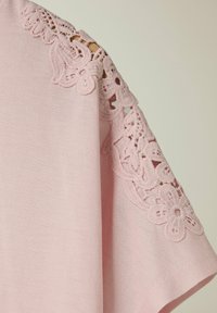 Ljust rosa topp med intrikata spetsdetaljer på axeln med blommönster, mjuk textur och avslappnad passform.