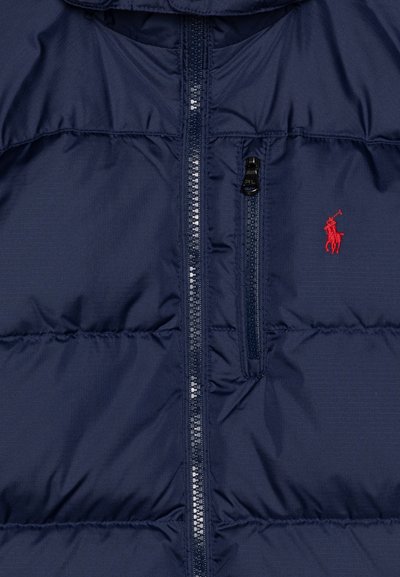 Veste matelassée bleu marine avec fermeture éclair à l'avant, une petite poche zippée et un accent logo rouge sur la poitrine, avec une texture lisse.