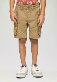 Shorts cargo beiges avec de multiples poches et des détails de couture. Portés avec des baskets blanches et grises ornées d'accents et de lacets bleus.