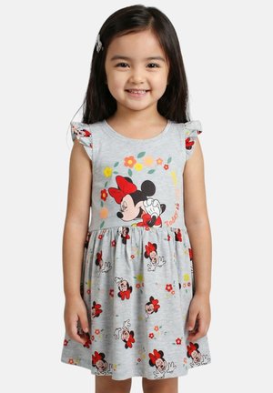 Jeune fille souriante, portant une robe grise avec des imprimés rouges et noirs de Minnie Mouse et des motifs floraux, et une barrette à cheveux sur le côté gauche.