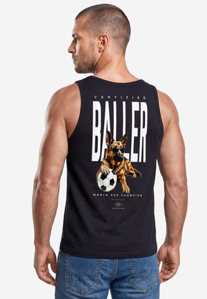 Mann mit kurzen Haaren, der ein schwarzes ärmelloses Shirt mit einem grafischen Hund, der Fußball spielt, und dem Text "Certified Baller" auf dem Rücken trägt.