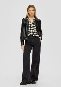 Zwarte leren motorjack over een blouse met houndstoothpatroon, gecombineerd met high-waisted donkere spijkerflared broek en chunky zwarte schoenen.