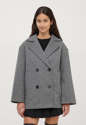Cappotto grigio doppiopetto realizzato in tessuto testurizzato, caratterizzato da grandi bottoni neri, ampi rever e una vestibilità larga e squadrata.