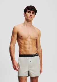 Hellgraue Boxer-Shorts mit einer weichen Textur, ausgestattet mit einem elastischen schwarzen Bund und einem Knopfdetail vorne.