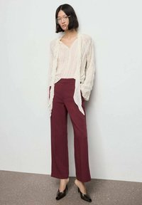 Blusa blanca, ligera y arrugada, combinada con pantalones burdeos de cintura alta y pierna ancha. Tacones negros de punta abierta completan el conjunto.