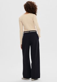 Maglietta beige a maniche lunghe abbinata a pantaloni neri a vita alta con gamba ampia, caratterizzati da una cintura in contrasto e tasche posteriori. Texture uniforme.