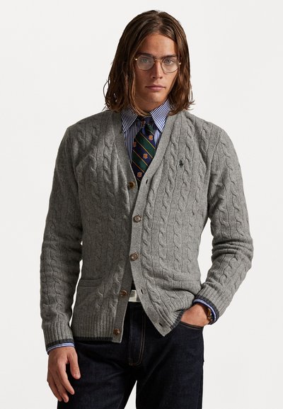 Grijze kabelgebreide cardigan met een V-hals, knoopsluiting aan de voorkant en twee voorzakken. Gecombineerd met een blauwgestreept shirt en een gebloemde stropdas.