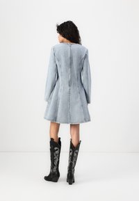 Denim haljina u svijetlo plavoj boji s dugim rukavima i lepršavim rubom. Ima vertikalni patentni zatvarač straga. Uparena s crnim čizmama do koljena u cowboy stilu.