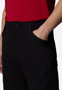 Black cargo pants featuring a button closure, side pocket, and textured fabric. The design includes a zippered pocket for added functionality.